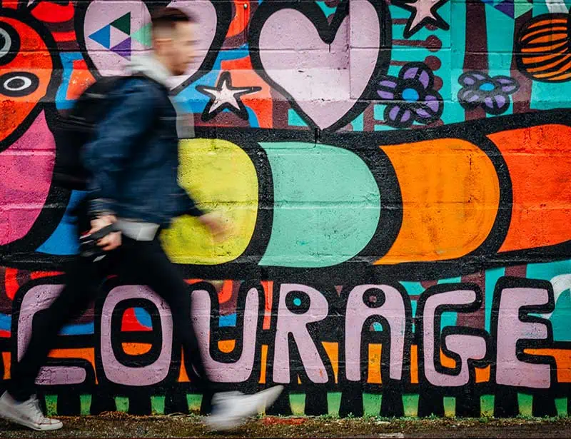 man walking in front of a colorful mural with the words courage