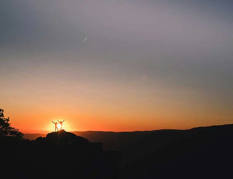 2 people silhouetted at the apex of a peak in yosemite.