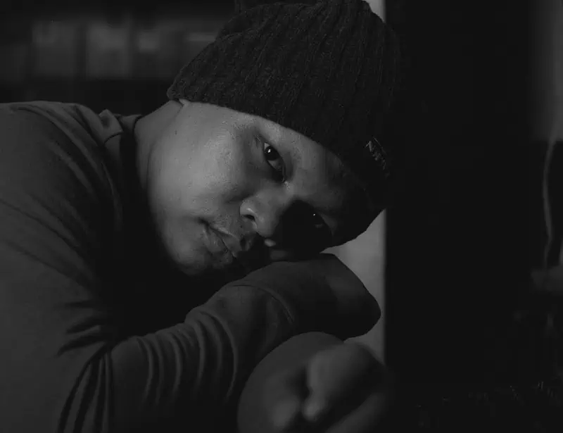 black and white closeup of black man wearing beanie while head on arms looking sad