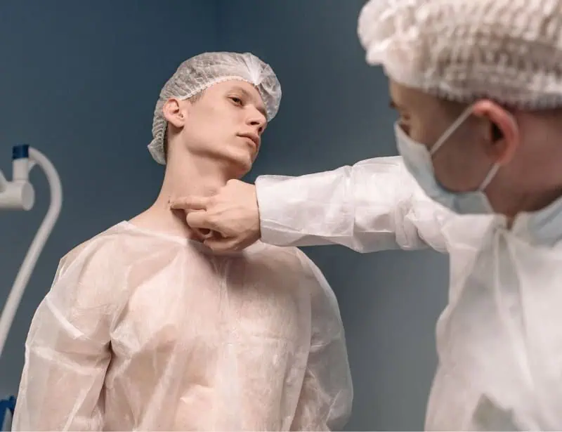 doctor touching neck of patient in clinic gown and cap