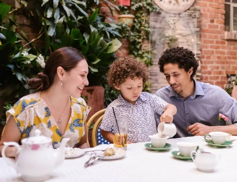 mother and father watching son pour drink in cup while dining outdoors