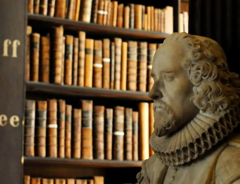 stone bust of William Shakespeare with shelf of old brown books at the back