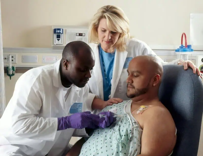 white nurse helping black doctor inserting chemotherapy tube to hispanic patient