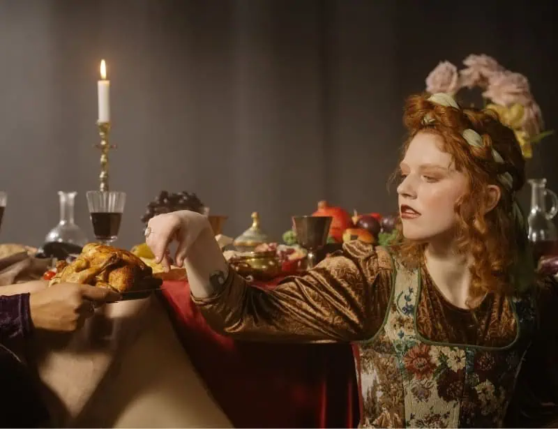 woman wearing renaissance period clothing with feast and candle at the back