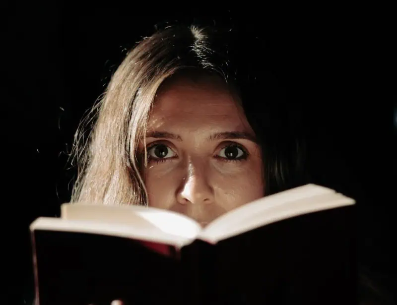 woman looking frightened while reading a book which is covering her mouth