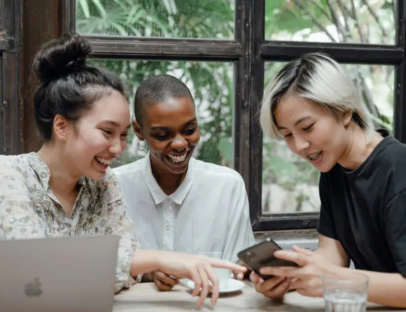 three women of different races smiling while using phone