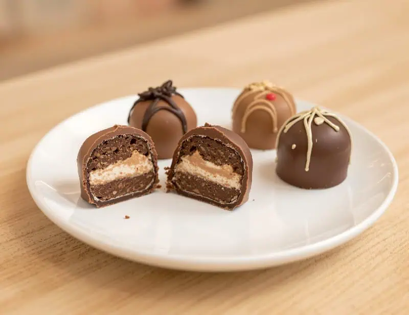 Gourmet chocolate bonbons arranged on a white plate displayed on a wooden counter in an artisanal chocolate shop.