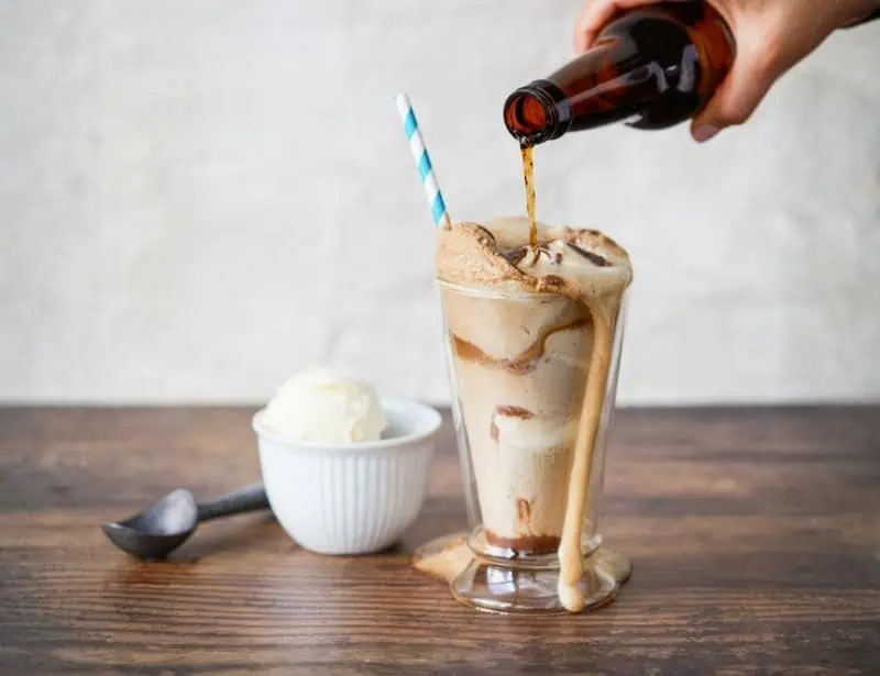 hand pouring root beer on tall glass with ice cream