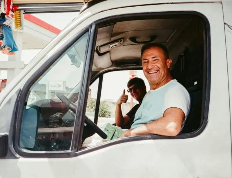 male trucker smiling and passenger doing thumbs up in white truck 