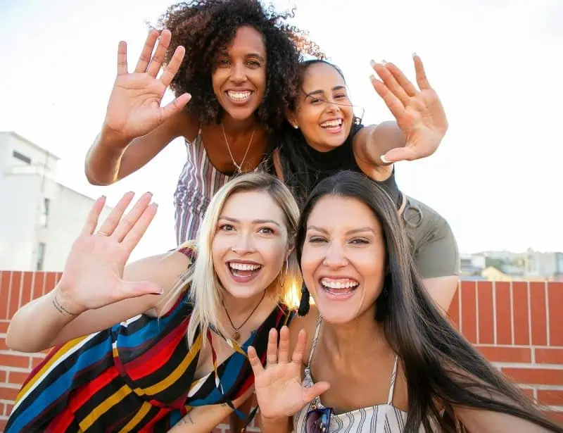 four diverse women waving to camera