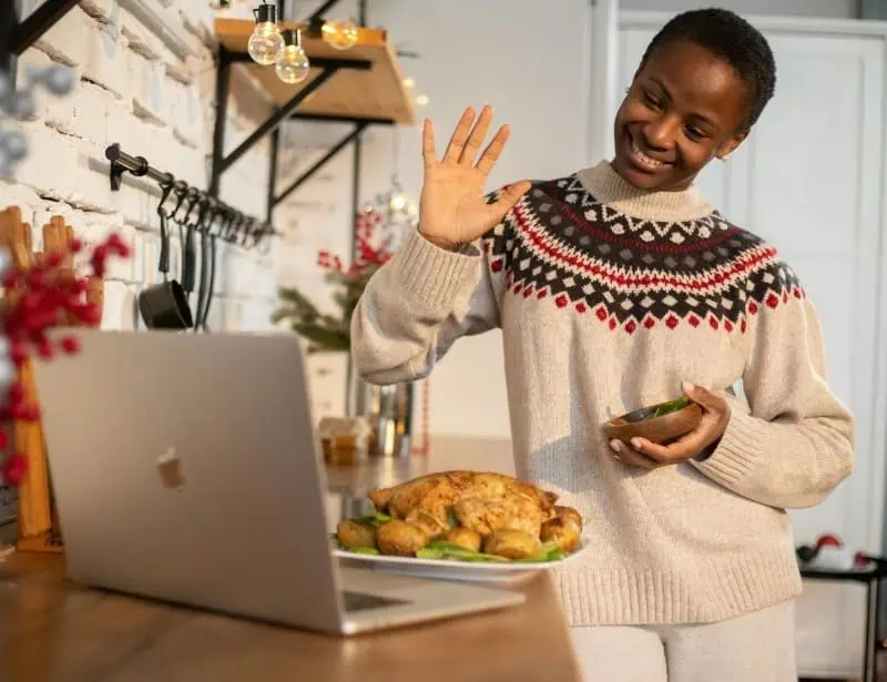 woman waving during video call showing cooked chicken