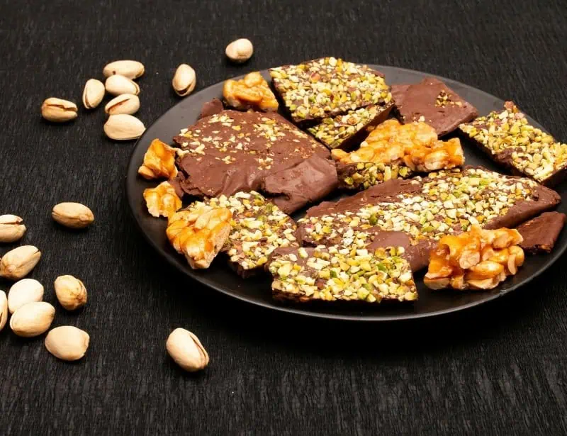 barks of varied nut brittles on black plate peanuts scattered on dark table