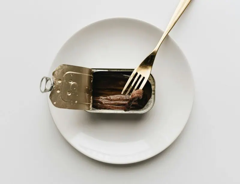 opened sardines tin on white plate with fork