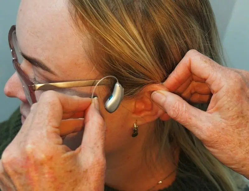 installation of silver colored hearing aid on blond woman with eyeglasses