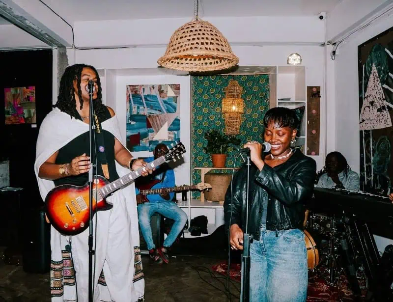 performing band in small room with man in guitar and woman as lead singer