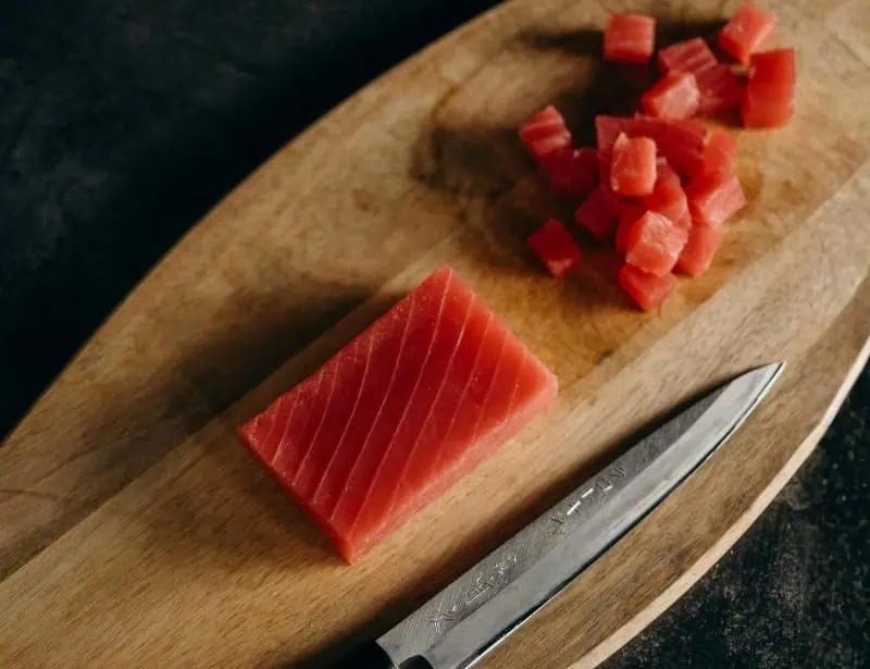sliced block of tuna on wooden board with knife