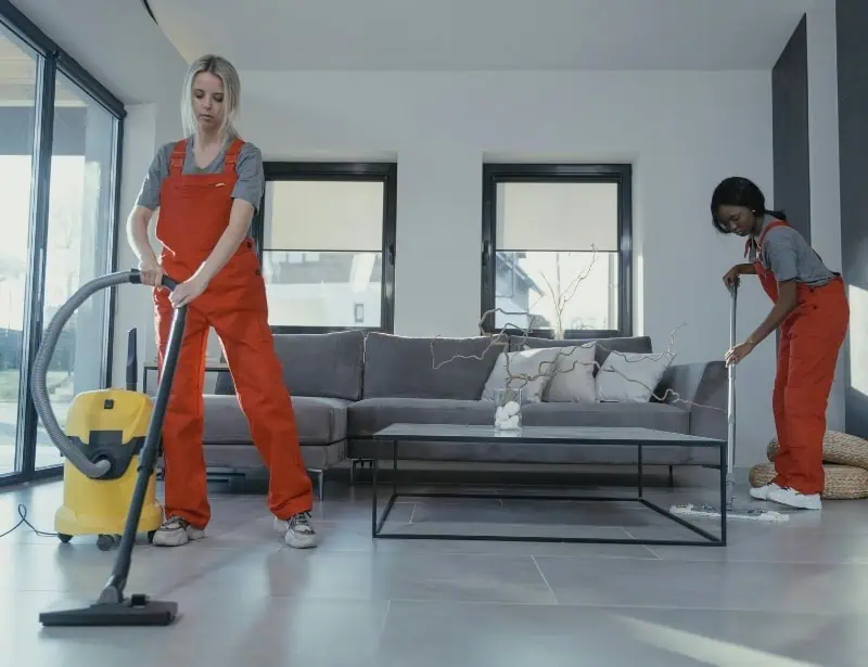 two female in red jumpsuit cleaning floor of living room