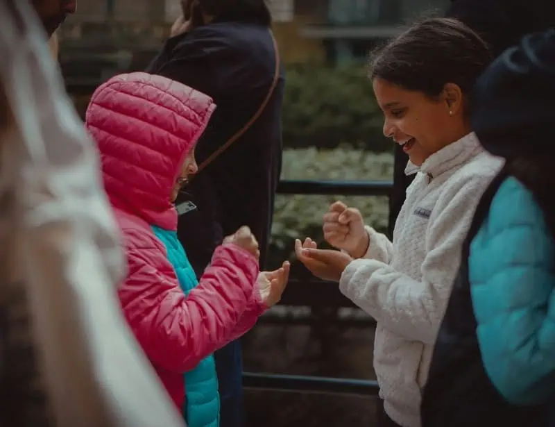 two young schoolgirls playing rock paper scissors in the middle of a crowd