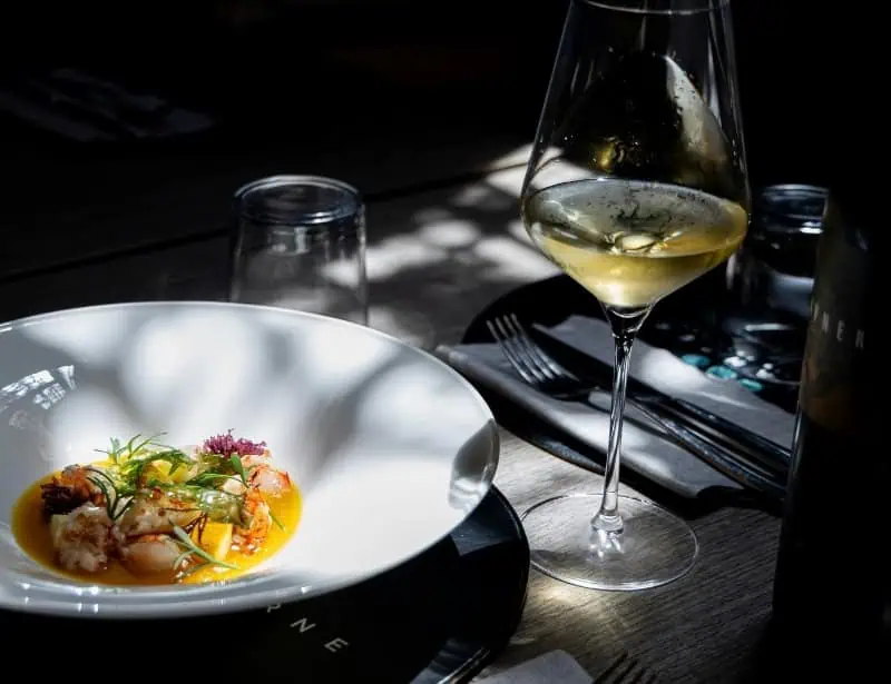 glass of white wine paired with colorful seafood dish on table with shadows