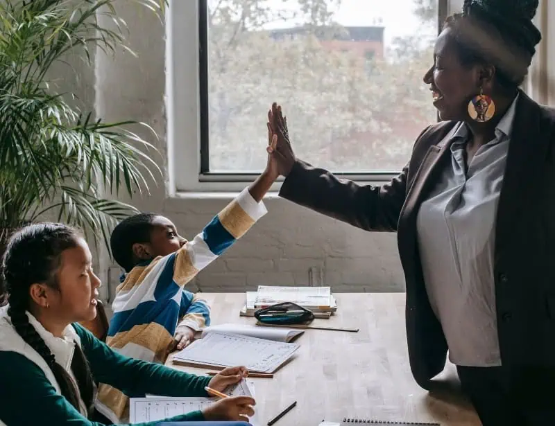 teacher doing high  five to one of -two young students doing writing exercises