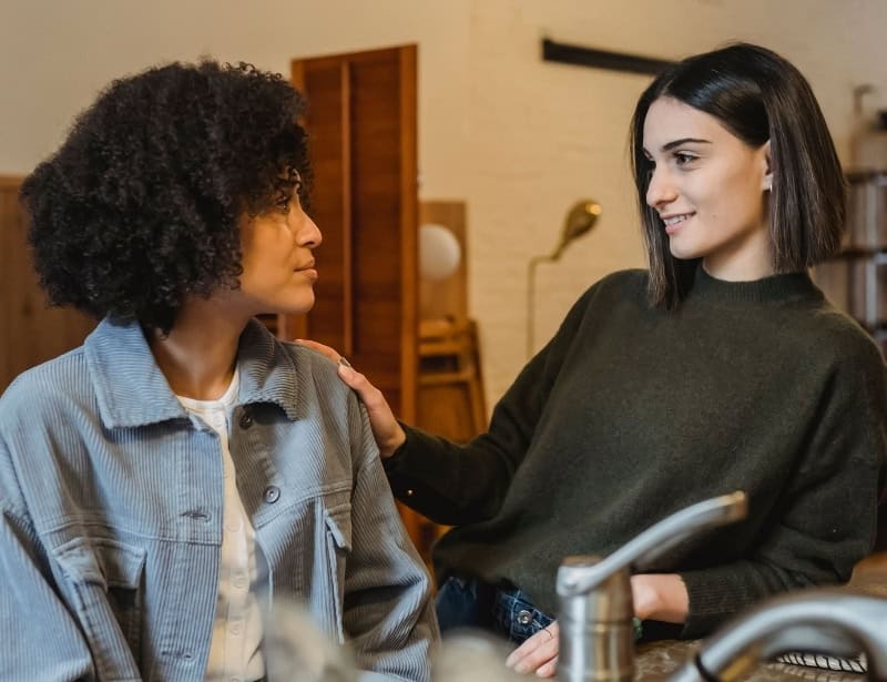 woman-smiling-putting-hand-on-shoulder-of-another-woman