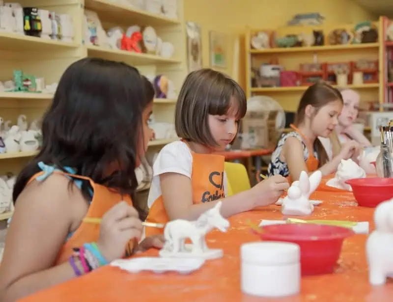 four young girls painting clay sculptures inside craft room