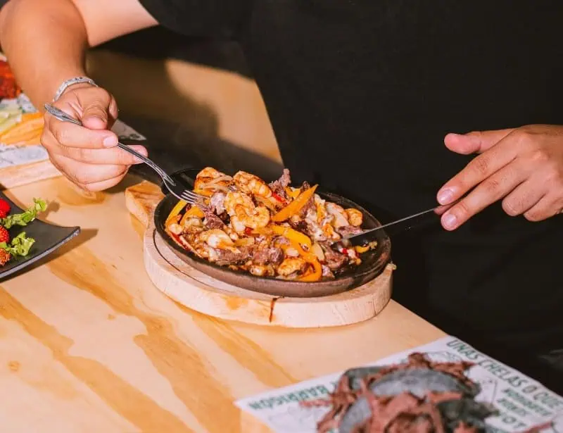 hands mixing beef shrimp fajita in sizzling plate