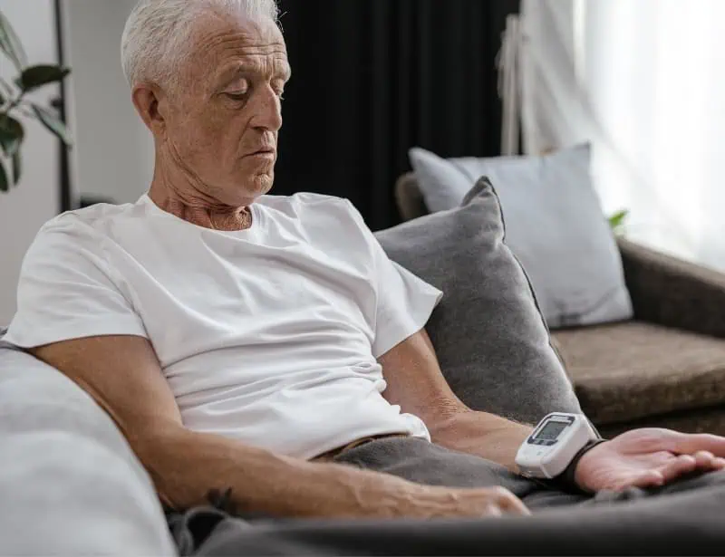 old man sitting on sofa checking blood pressure with wrist device