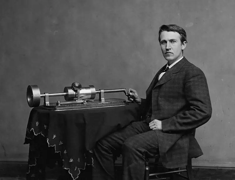 thomas edison siiting beside his phonograph invention in black and white