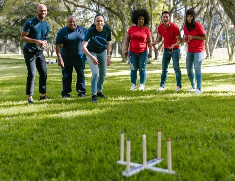 adults separated into blue and red team playing ring toss in the park 