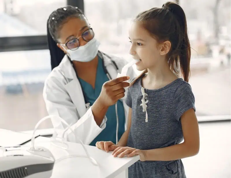 black female doctor with mask helping small girl breathe with nebulizer 