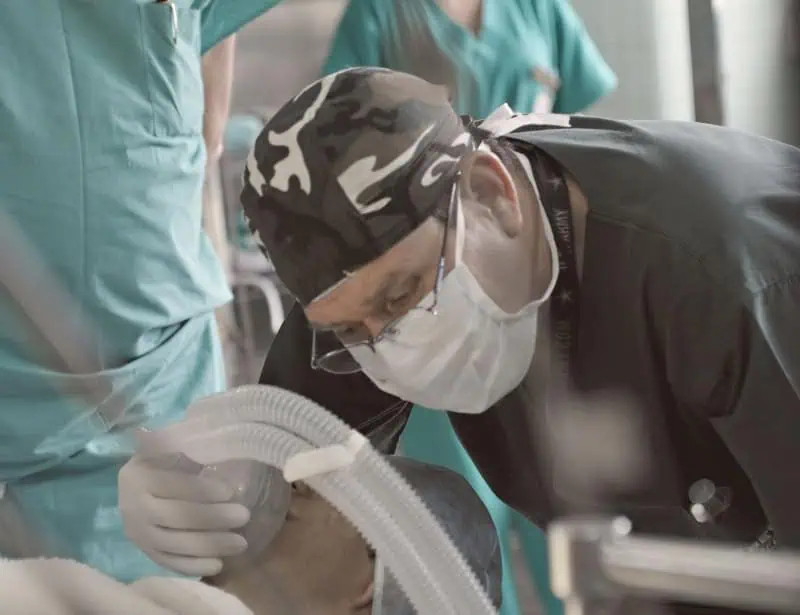closeup of doctor with face mask and eyeglasses installing breathing apparatus to patient 