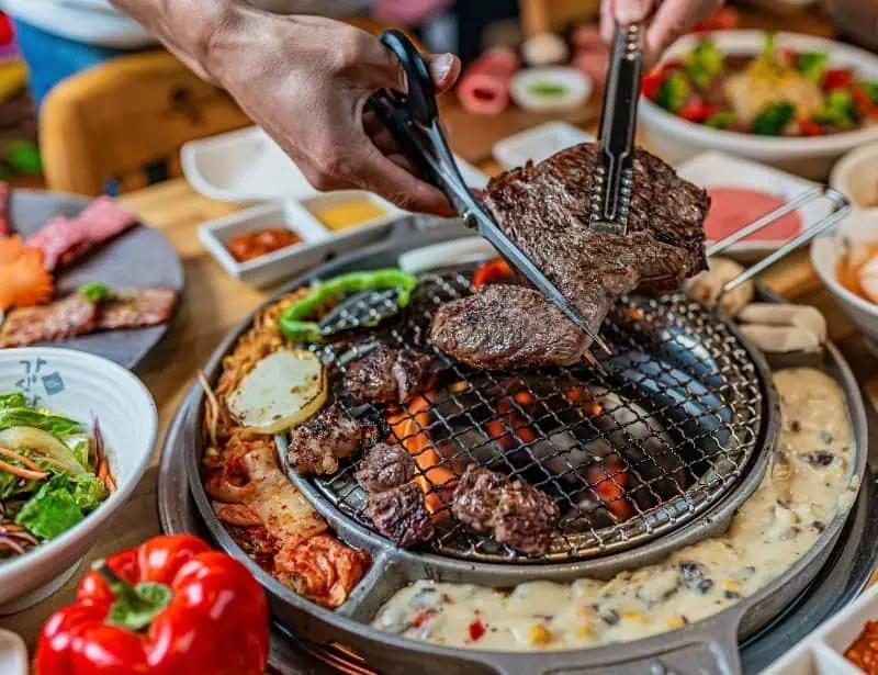 colorful spread of korean barbecue with side dishes and cutting meat with scissors