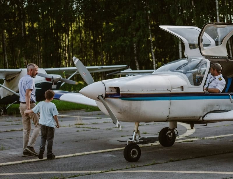 father showing son a parked white light aircraft with pilot inside 
