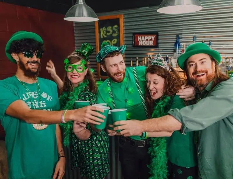 five adults wearing green shirt with other green accessories celebrating st patricks with drinks in green cup