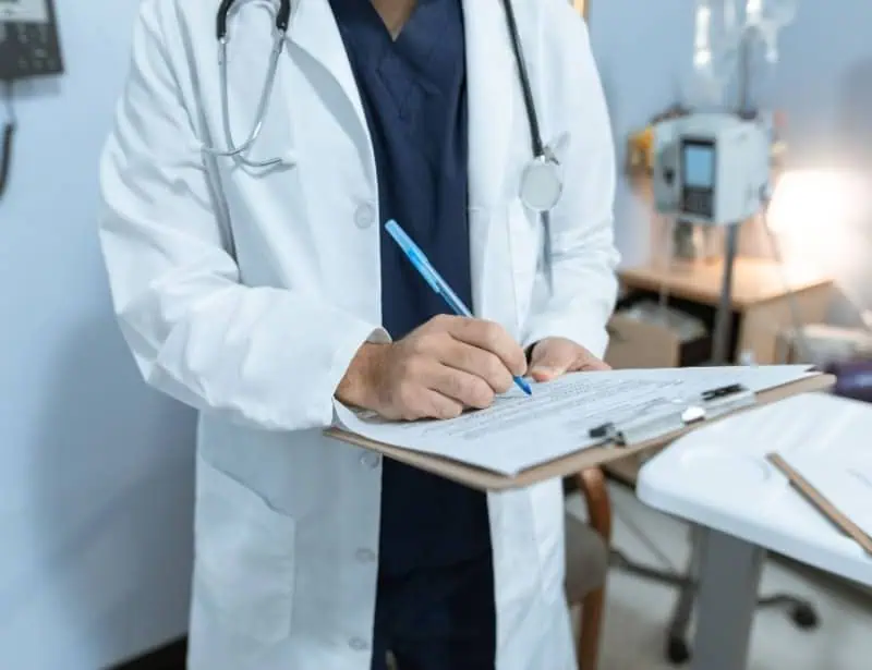 focus on doctor with stethoscope hanging around neck writing on paper attached to clipboard 