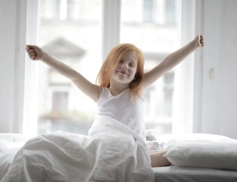 girl with red hair waking up smiling on white bed in white room 