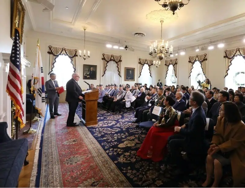 governor hogan talking to koreans and americans in maryland statehouse with first lady at the front and two countrys flags at back of mayor