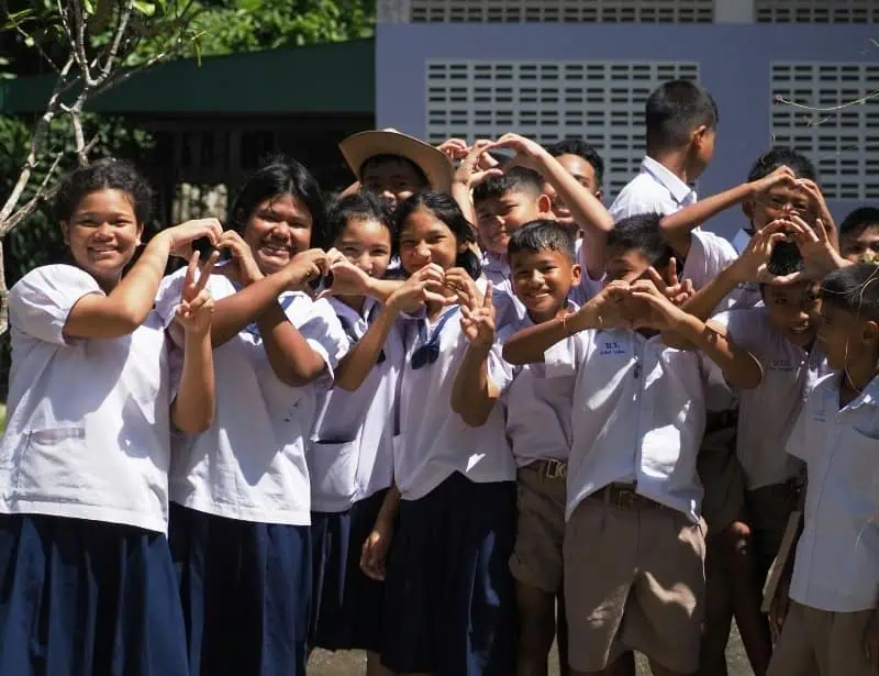 group of southeast asian kids in uniform smiling and forming hearts with hands 