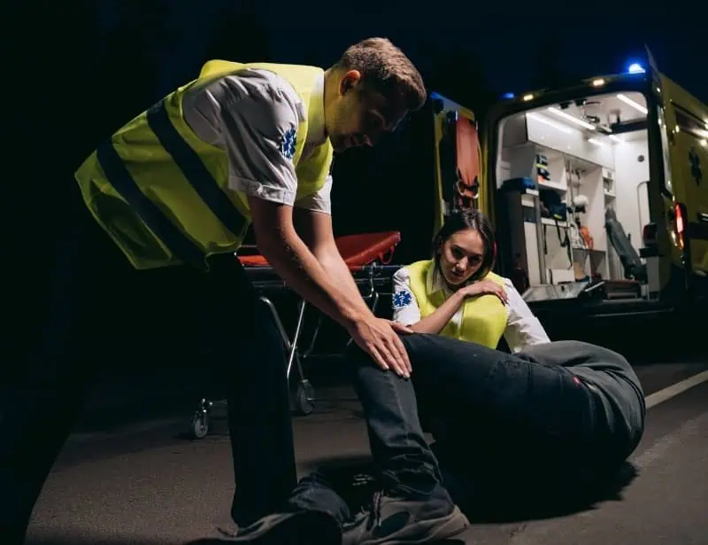 paramedics moving man to his side with ambulance at back
