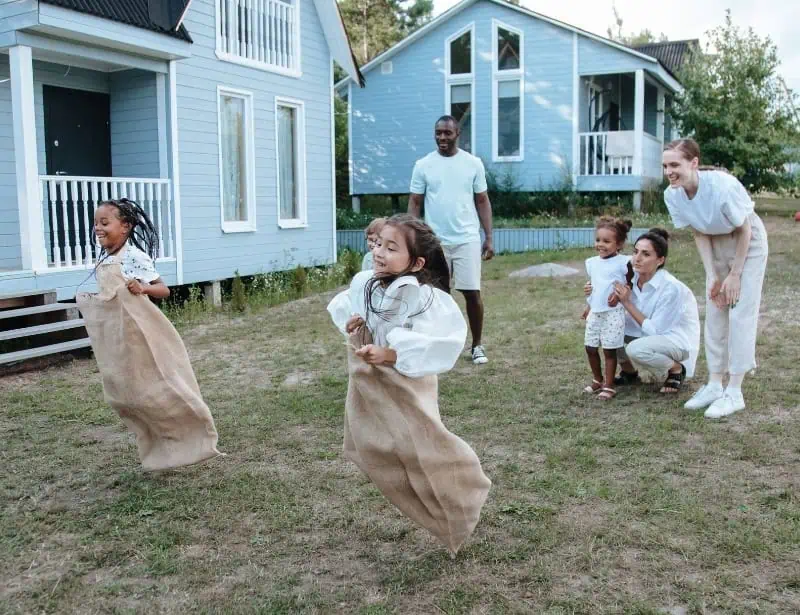 parents and child wearing white clothes playing sack race in backyard 