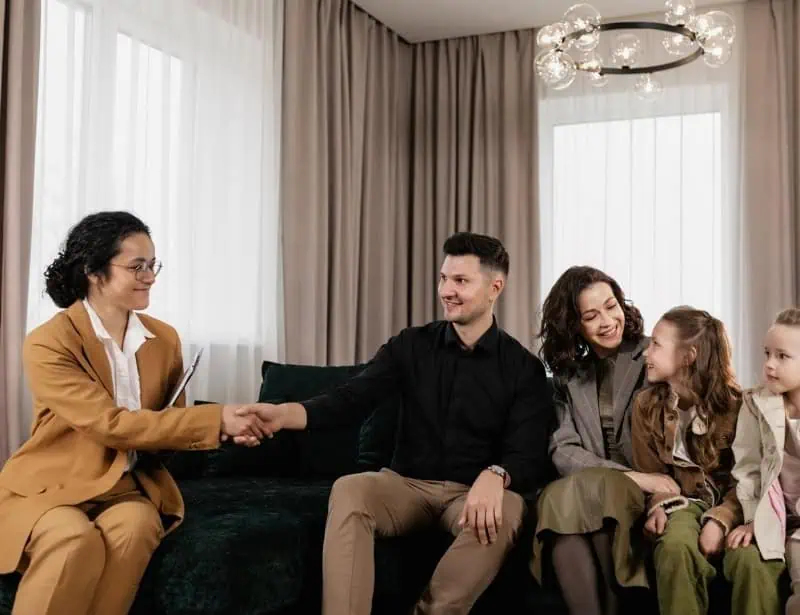 woman in light brown suit shaking hands with father mother and daughter looking at each other