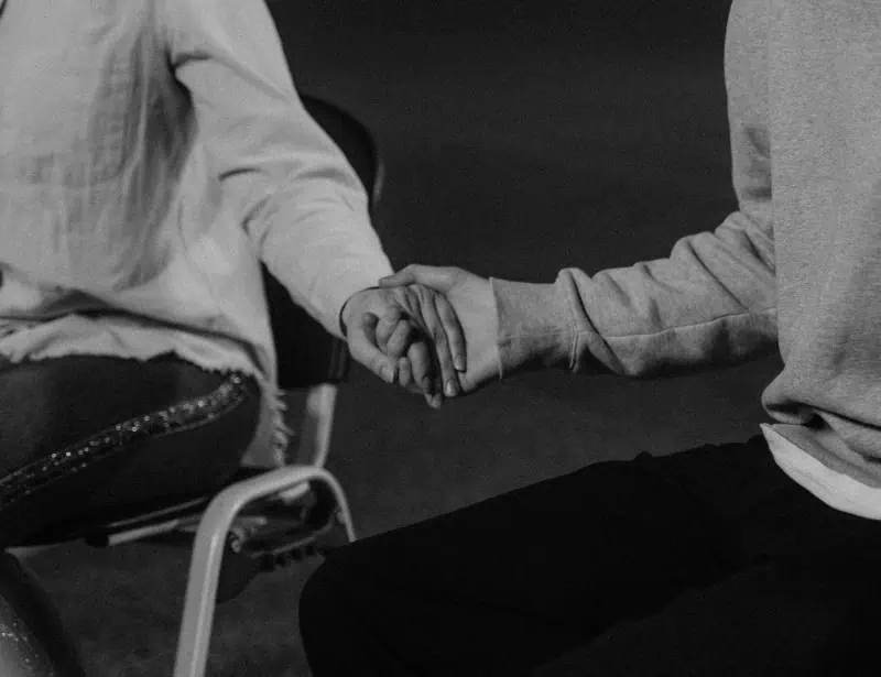 black and white closeup of two sitting person holding hands 