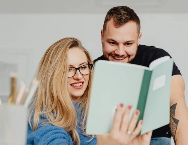 blond haired woman showing smiling man something from her green notebook