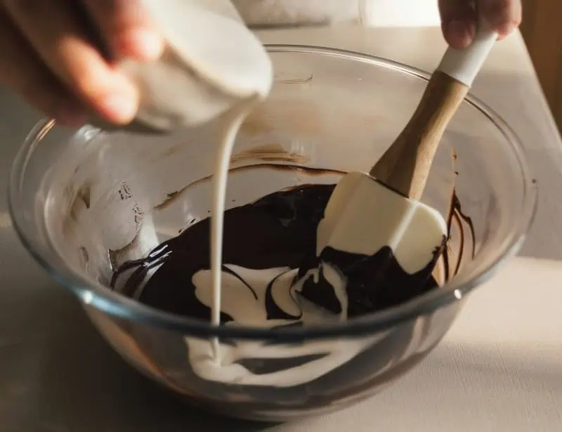 hand mixing melted chocolate and cream with silicone spatula in glass bowl