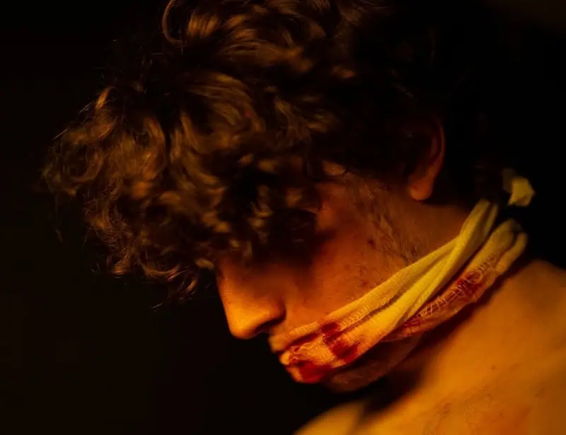 man head down with mouth covered with white blood stained cloth 