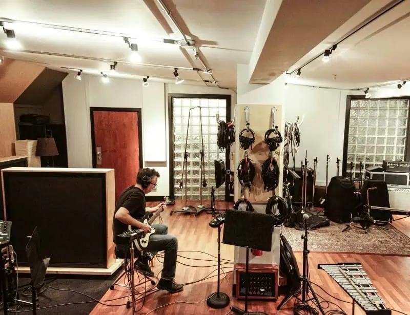 man playing electric guitar in the middle of music studio full of instruments
