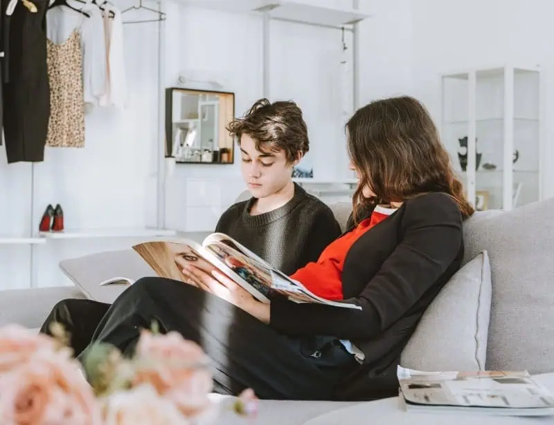 mother and son looking at magazine while sitting on sofa